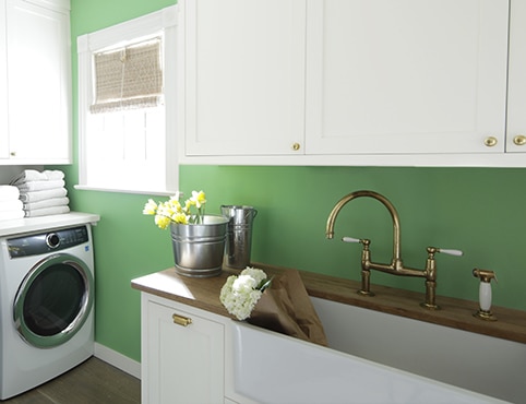 Una habitación de lavado con gabinetes blancos y una pared pintada de verde con mesada de madera y lavadora y secadora blancas.