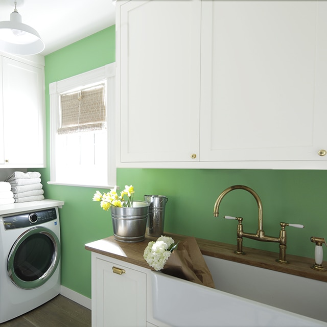 Une salle de lavage arborant des armoires blanches, un mur vert, un comptoir en bois ainsi qu’une laveuse et une sécheuse blanches.