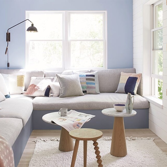 A bright, cheerful periwinkle painted living room with a white side wall and trim, a large banquette sectional with a gray base, and three small tables.