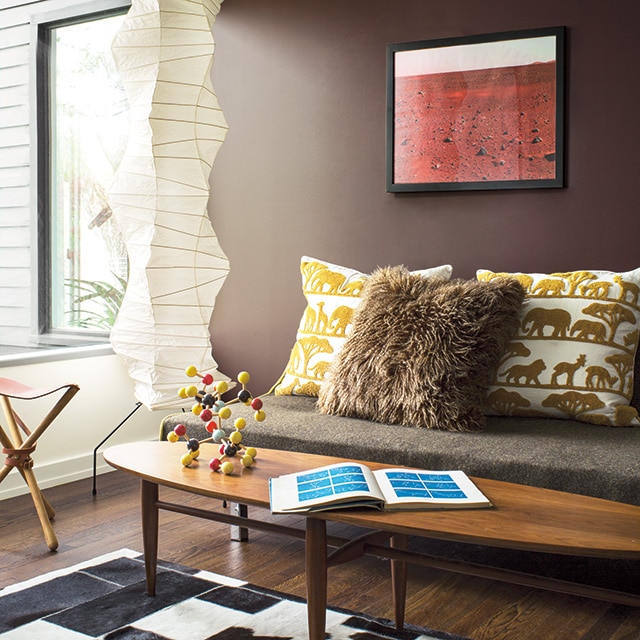 Salon éclectique avec un mur brun derrière un sofa, un mur latéral blanc et des accessoires à motifs d’animaux. 