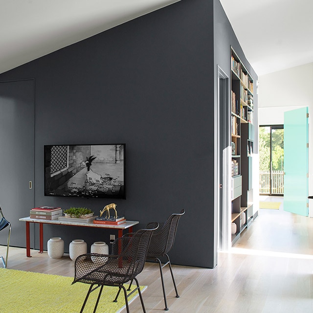 A bright, open living room area with black accent walls and door, a white vaulted ceiling and walls, modern furniture, and a light blue door at the end of a hallway.