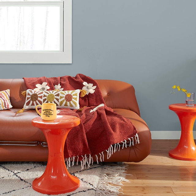 A fun, retro-style living room with a blue-gray painted wall, white trim, a brown leather couch, and two orange tables.
