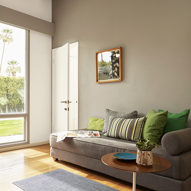 A sunlit living room with a taupe-painted accent wall, white wood beamed vaulted ceiling, a white door and modern style furnishings.