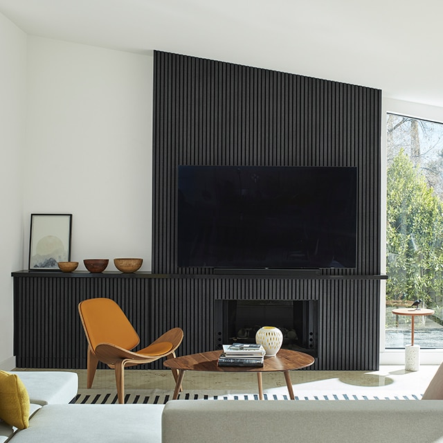 A mid-century modern style living room with bright, white-painted walls and vaulted ceiling, and a black panelled accent wall, built-in cabinet and fireplace, and large screen TV.