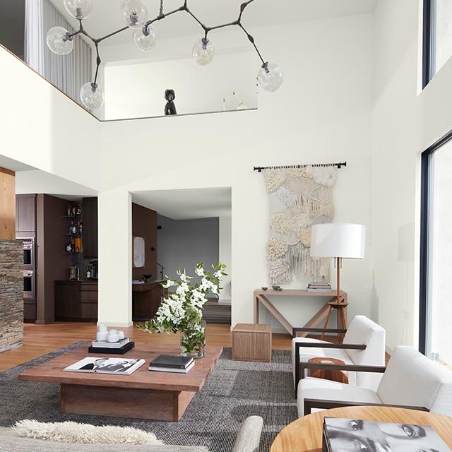 A bright open, white-painted mezzanine style living room with modern white and wood furnishings, a hanging light fixture, and dark brown and gray far walls.