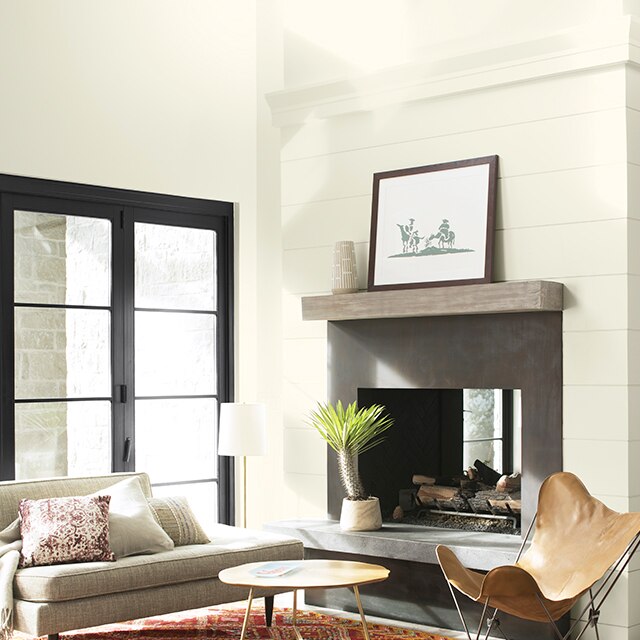 A white-painted living room with vaulted ceiling, fireplace, modern furniture, layered orange and red area rugs, and black French doors. 