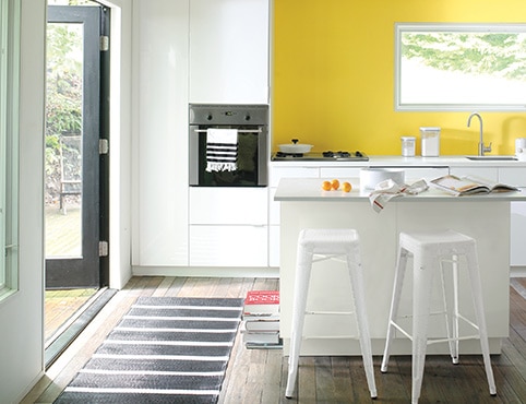 A modern kitchen with a navy blue and white striped floor runner and a bright yellow-painted accent wall.