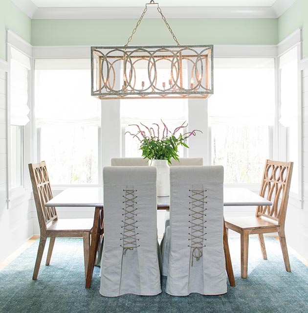 Paredes de comedor en verde suave con revestimiento con paneles de madera pintados de blanco que ocupan los 3/4 inferiores de la pared.