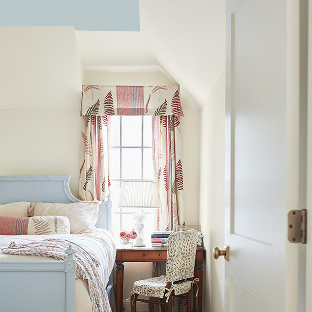 Une chambre à coucher aux murs en blanc cassé et au plafond peint en bleu clair arborant un cadre de lit assorti.