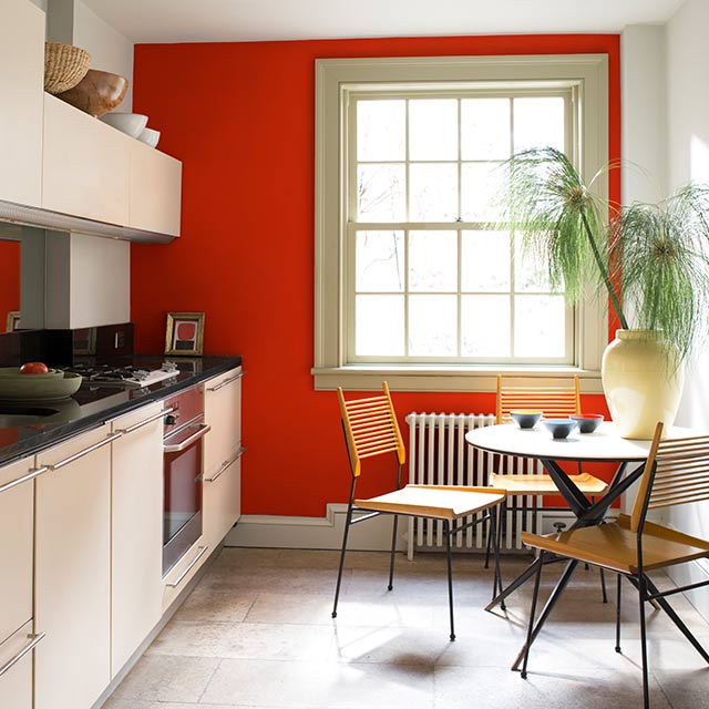 White kitchen cabinets with black countertops and a vibrant, red-painted accent wall. 