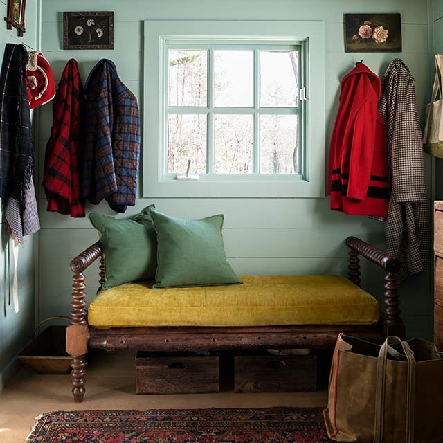 A mudroom with light green walls and ceiling with a yellow bench and red oriental rug.