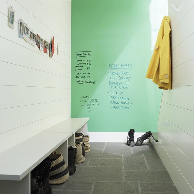 A large mudroom with white shiplap walls, a long bench, and a green dry erase accent wall.