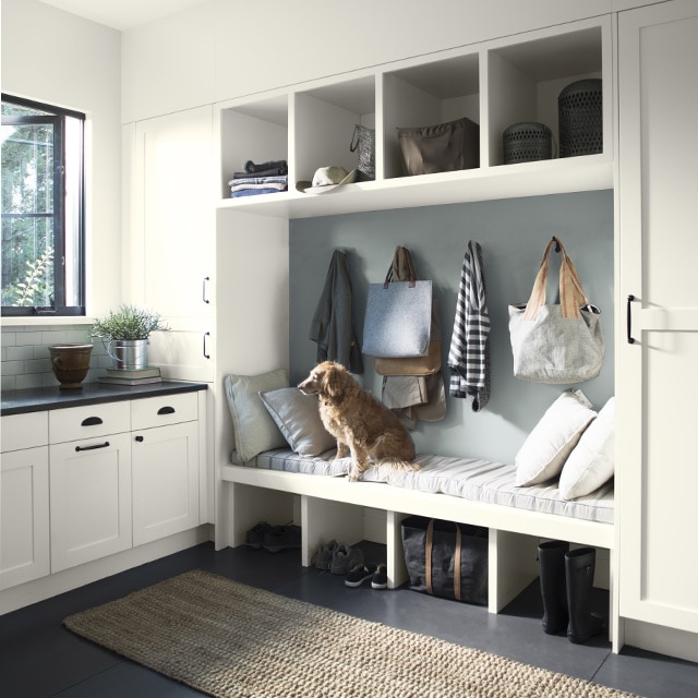 Open mudroom with dark floors and white walls with a built in cabinet and wall seating.