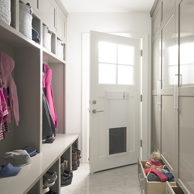 An off-white mudroom with floor to ceiling cabinets across from a wall bench and overhead cubbies.