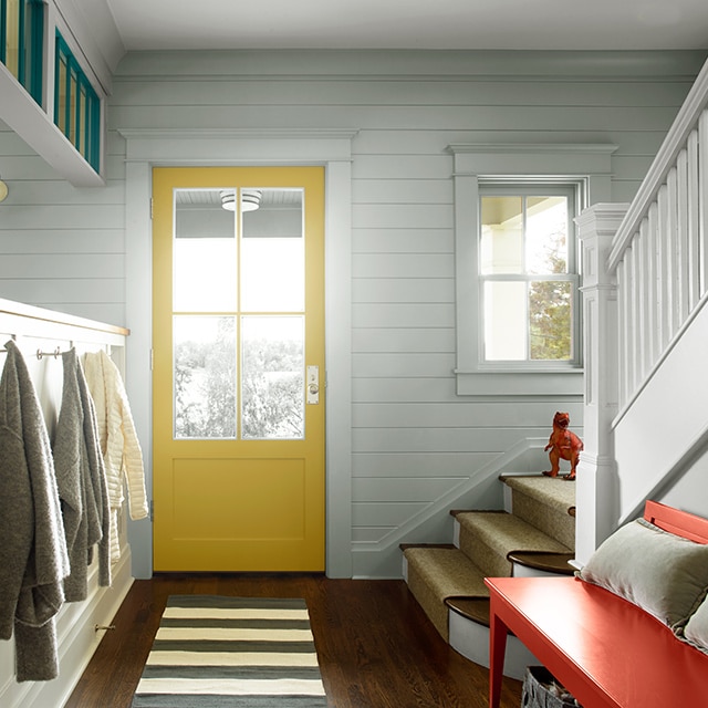 Gray mudroom with a yellow door, gray built in cabinets next to a striped gray and white floor runner.