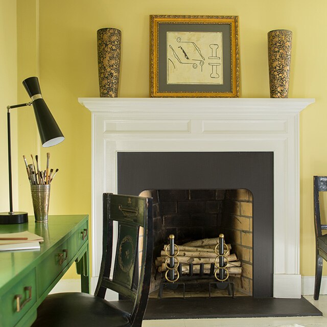 La jolie table de travail verte et l’élégante chaise noire se découpent à merveille dans cette pièce peinte en jaune avec un manteau de cheminée blanc et un petit tapis aux motifs abstraits noir et blanc.
