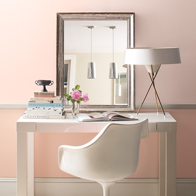 Bureau blanc moderne avec chaise, lampe et miroir devant un joli mur rose à deux tons avec moulures blanches.