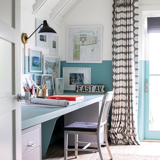 A cheerful home office with white painted upper walls, a vaulted ceiling with beams, and blue painted lower walls and desktop.