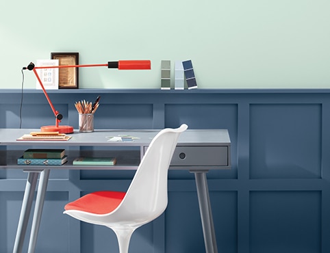 A home office with a light blue painted upper wall, dark blue wainscoting, a modern gray desk, and a white chair.