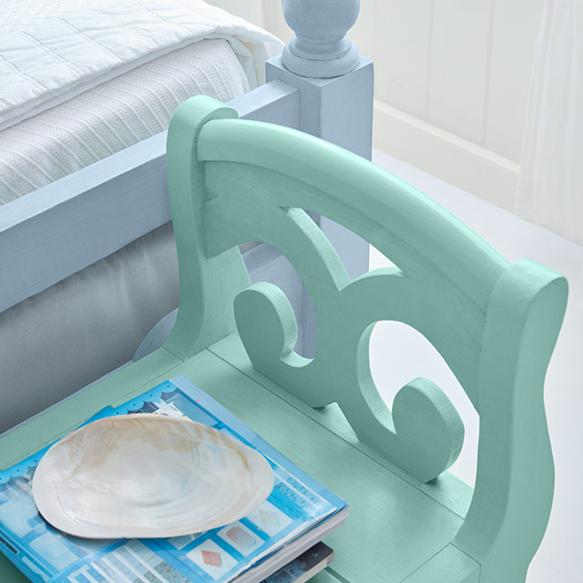 Coin d’un cadre de lit en bois bleu pâle avec banc turquoise posé devant et mur blanc.