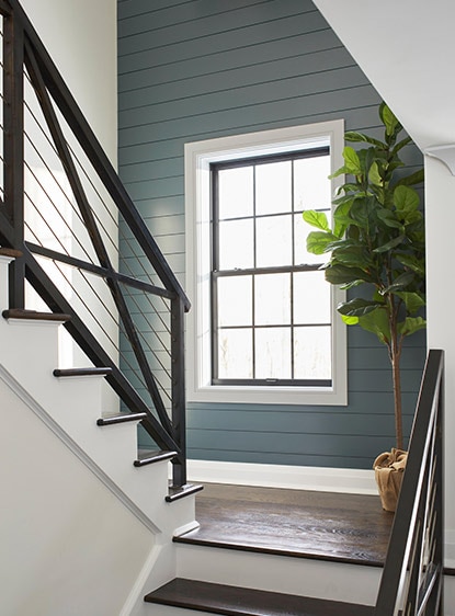 Escalera de madera con pasamanos de metal negro en una habitación blanca con una pared de acento gris azulada.