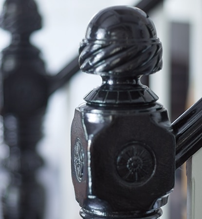 A close-up of a intricately carved staircase newel in high-gloss black paint.