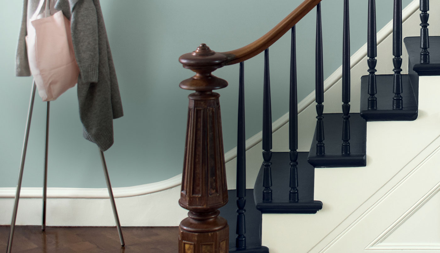 Escalier d'entrée avec rampe et pilastre de départ en bois et marches peintes en bleu marine.