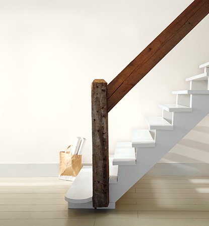 Pièce lumineuse et aérée avec escalier blanc et rampe en bois naturel.