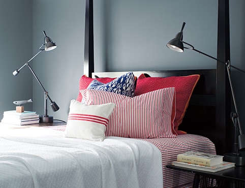 Sleek, Wolf Gray-painted bedroom with black bedframe, red and white bedding, two swing-arm lamps, and stacks of books.