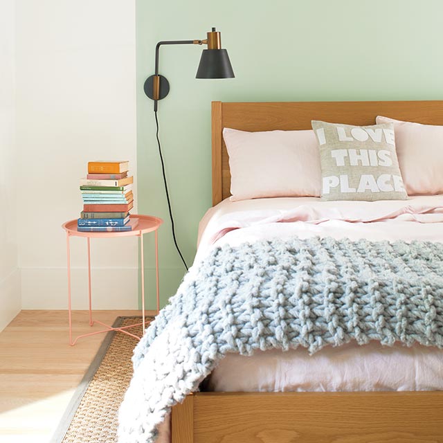 Une chambre blanche arborant un carré peint en vert derrière un lit en bois.