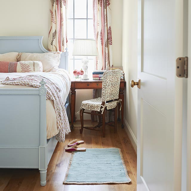 White-painted bedroom with blue ceiling and bed frame, and a wooden accent chair.