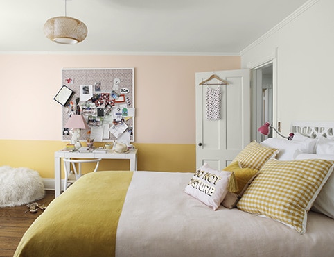 Pink-and-yellow-painted bedroom with beanbag chair, corkboard, white desk and bedspread with two-toned bedding.