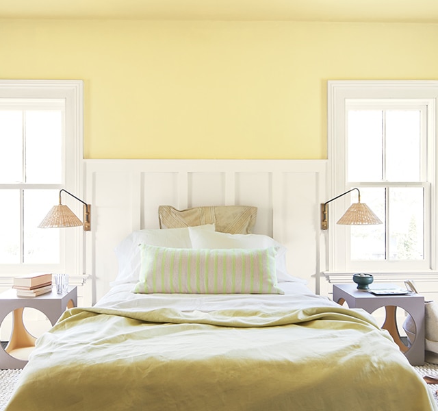 Chambre à coucher lumineuse avec lambris d’appui blanc cassé, murs jaunes et fenêtres aux boiseries blanches.