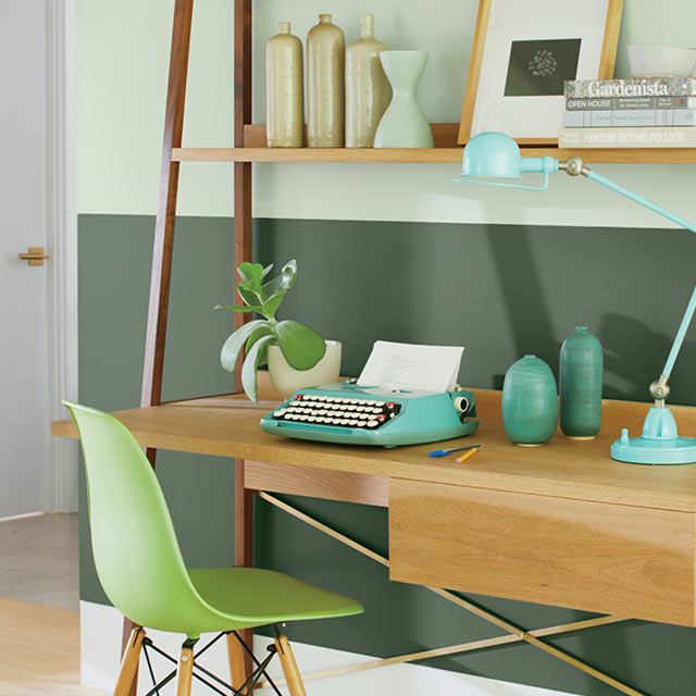 An office with a two-tone green painted wall, a white door, a modern desk with shelves and coloured vases, and a green chair.