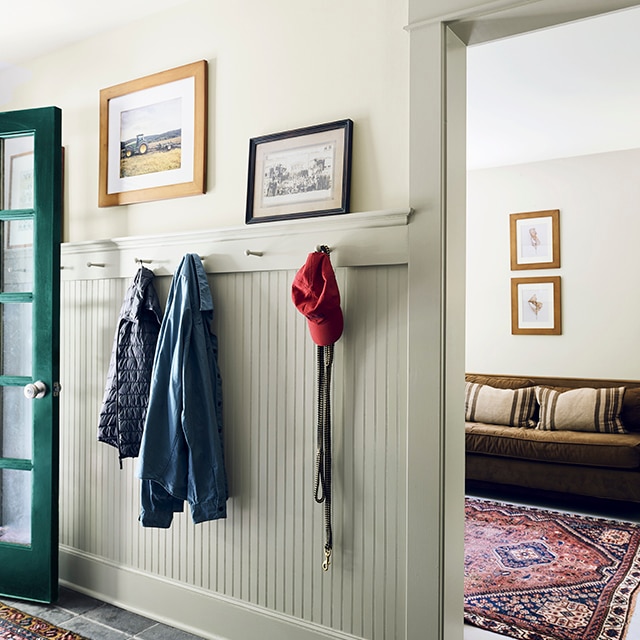 A pale green-painted entry hallway with dark green front door, area rug and a cozy seating area in neutral tones seen through an open doorway.