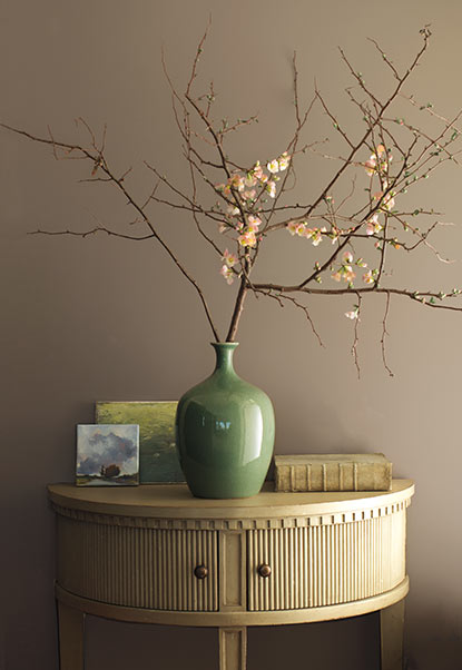 Minimalist floral arrangement in green vase against gray-brown wall.