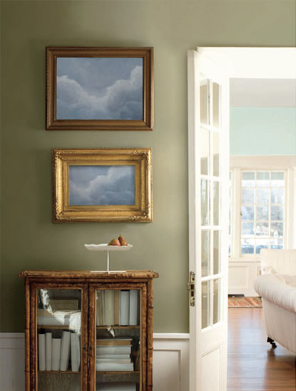 A soft, neutral green accent wall framed by a wooden console