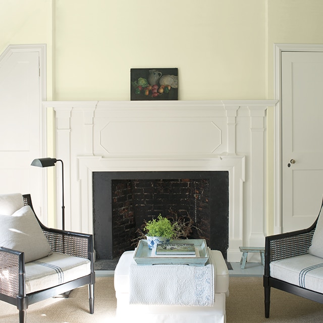 Joli mur jaune-vert avec cheminée blanche flanquée de deux portes blanches avec deux fauteuils et un pouf blanc.