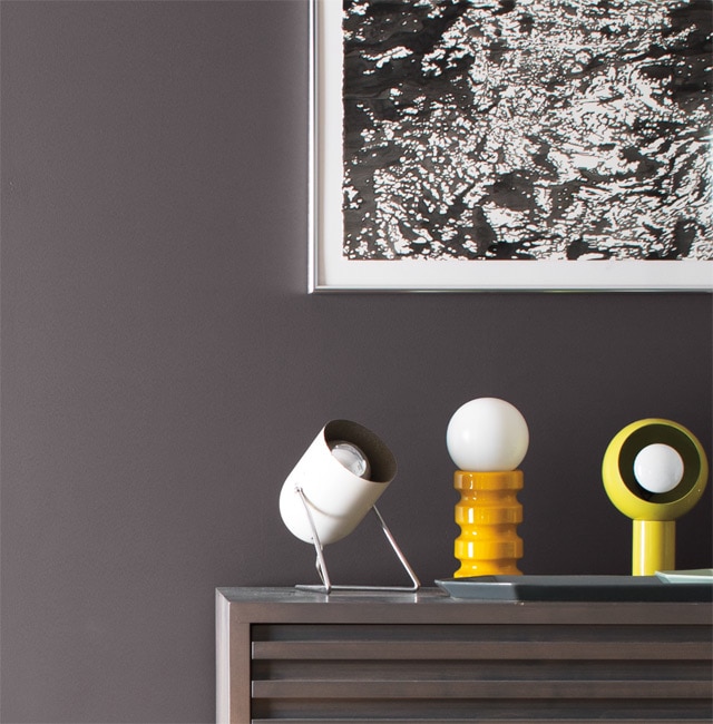 Three small lighting fixtures atop a bureau are set against a grey wall underneath a black and white photograph.