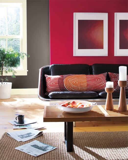 This casual living room includes a mod leather couch, slatted wooden coffee table, bold graphic framed prints and a bold, red-colored accent wall.