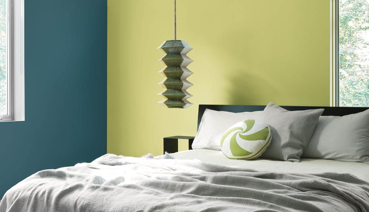 A bedroom with two painted walls, one in Lilianna CSP-855, a soft yellow-green, and the other in Stained Glass CSP-685, an aquatic deep blue. 
