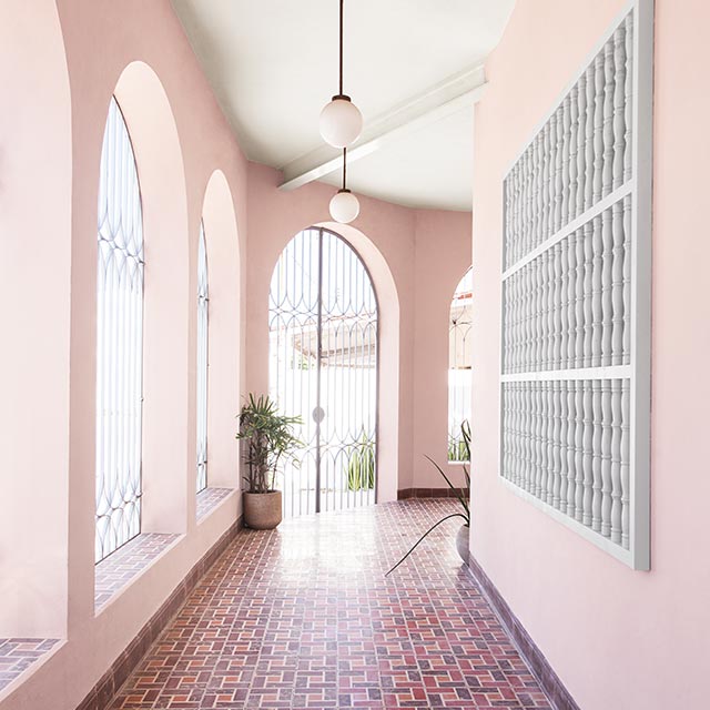 Galerie couverte aux murs roses, plafond blanc, fenêtres en arc, unité murale en forme de grillage de fenêtre gris pâle et plancher en carreaux de céramique de plusieurs teintes de rouge.