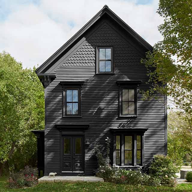Maison et porte d’entrée peintes en noir avec des arbres de chaque côté.