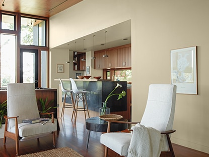 Chaise rembourrée blanche dans un salon et une cuisine neutres, avec des murs de couleur beige et des armoires en bois.