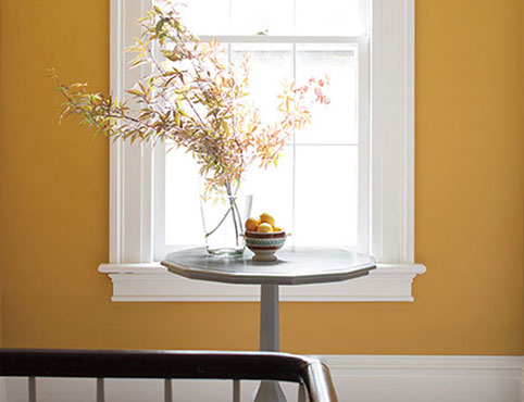 Yellow-painted hallway with wooden table and flowers, two doors, a window, and white-painted trim.