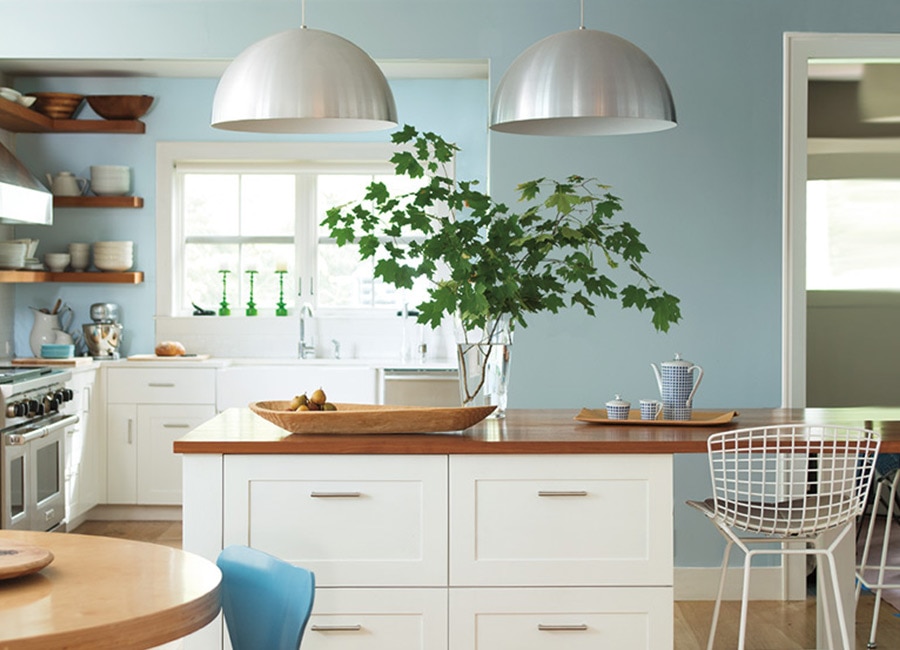 Modern kitchen with overhead lighting, light blue-painted walls, white counters and metal seating.