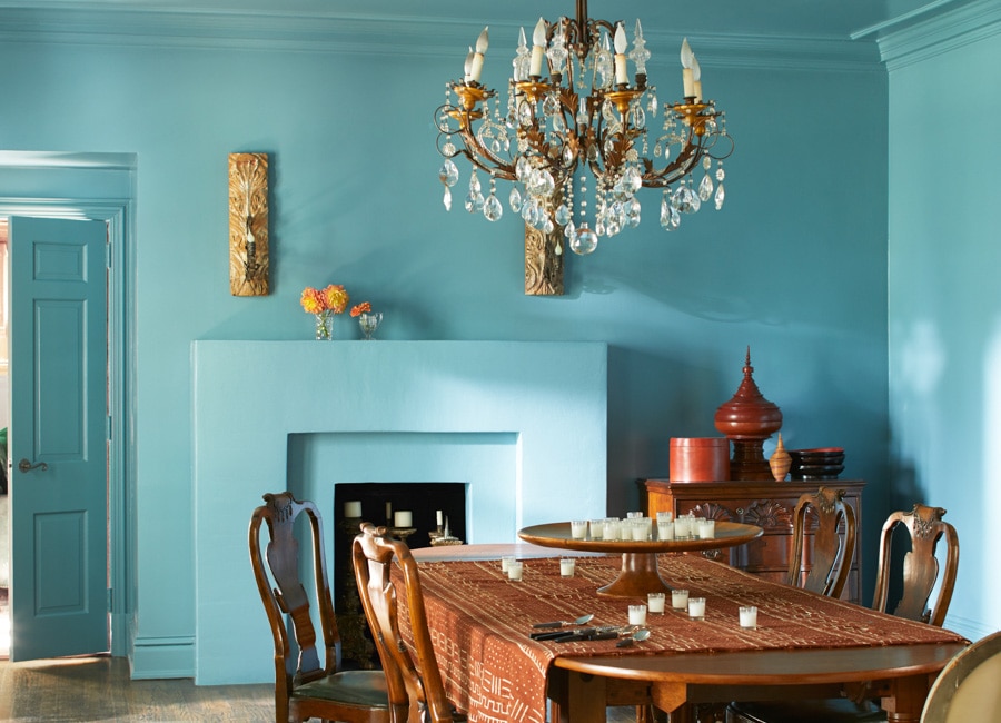 Une somptueuse salle à manger arborant des murs, un plafond et un foyer bleus, ainsi qu’un lustre suspendu au-dessus d’une grande table et de chaises en bois. Un style classique doté d’une touche d’exotisme.