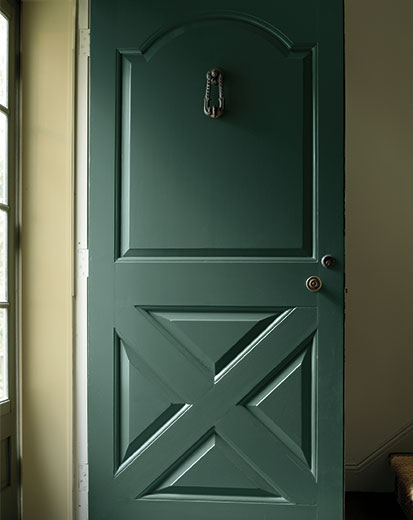 Entrada con puerta principal en verde oscuro y paredes interiores en verde claro.
