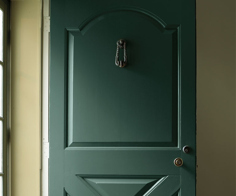 Un hall d’entrée arborant une porte vert foncé et des murs intérieurs vert clair.