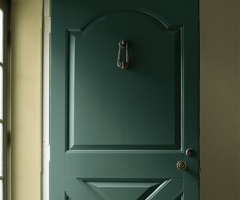 Entrada con puerta principal en verde oscuro y paredes interiores en verde claro.